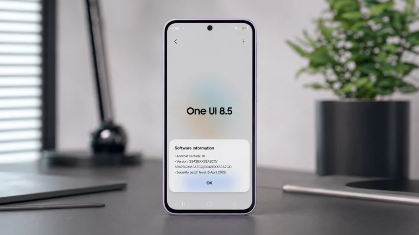 Lavender Galaxy A37 standing upright on a matte professional tech table with the One UI 8.5 software information screen open, a blurred plant, desk lamp, and clean workspace background behind it.